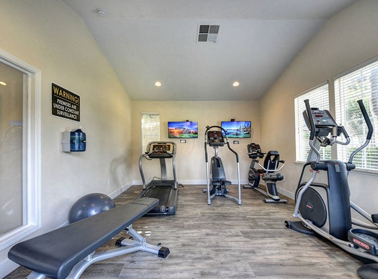 Apartments for Rent Rocklin - Fitness Center with Multiple Machines, Large Windows, and Two TVs.